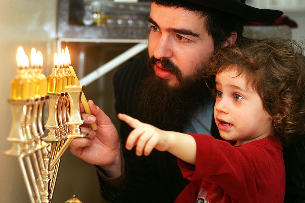 Jewish man and child lighting menorah